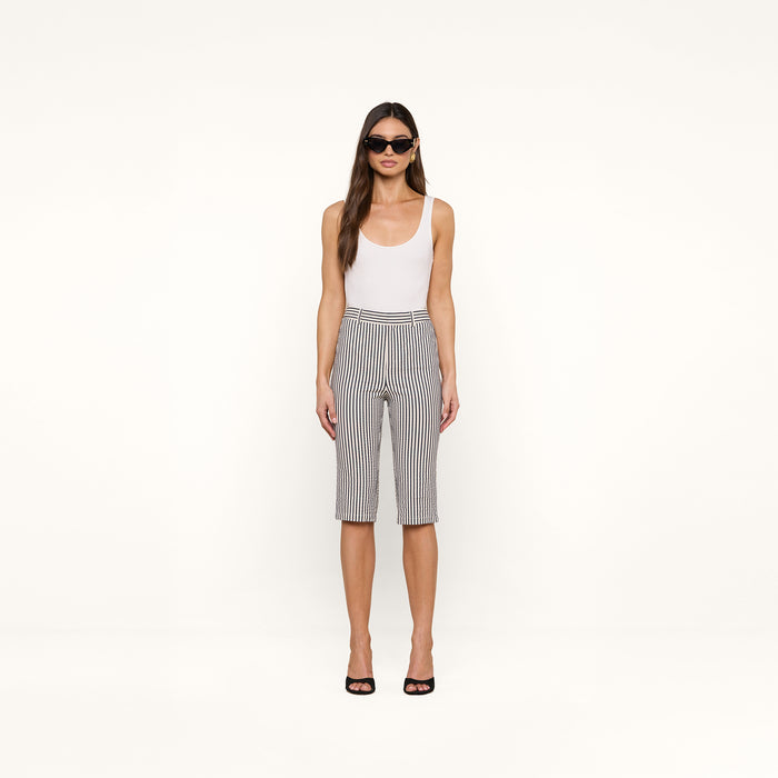 A woman stands facing forward against a plain white background, wearing sunglasses, a white tank top, and the Leni Pedal Pusher in black and white stripes.