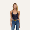 A woman with long blonde hair wears the Lexi Silk Camisole in midnight blue, paired with blue jeans, a beige belt featuring a gold buckle, and hoop earrings. She stands against a plain light background, facing the camera with a neutral expression.