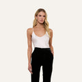 Wearing the Lexi Silk Camisole in white with adjustable straps and black pants, a woman stands with one hand in her pocket against a plain light background.