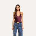 A woman with long brown hair is wearing the Lexi Silk Camisole, a bias-cut silk top with adjustable straps, paired with blue jeans and a belt, standing against a plain, light background.