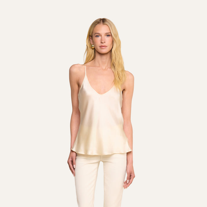 A woman with long blonde hair models the Lexi Silk Camisole in pearl white, paired with matching cream pants, standing against a plain light background and looking directly at the camera.