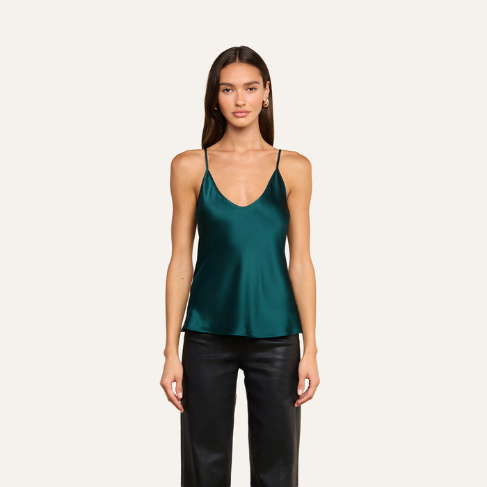 A woman wearing the Lexi Silk Camisole in dark green, featuring a bias-cut design and adjustable straps, paired with black leather pants, stands facing forward against a plain light background.