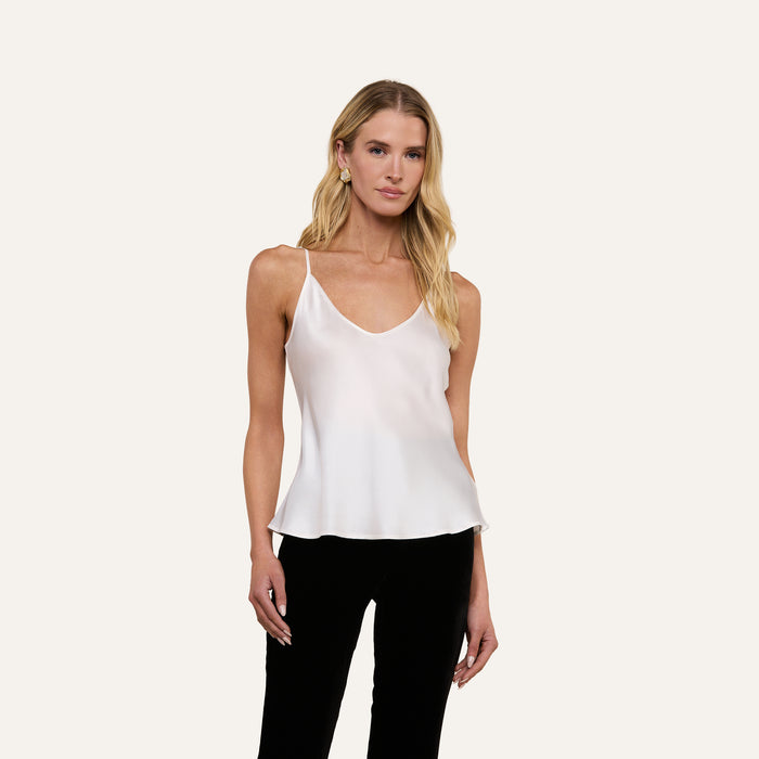 A woman with long blonde hair wears the Lexi Silk Camisole in white, featuring adjustable straps, paired with black pants while standing against a plain light background.