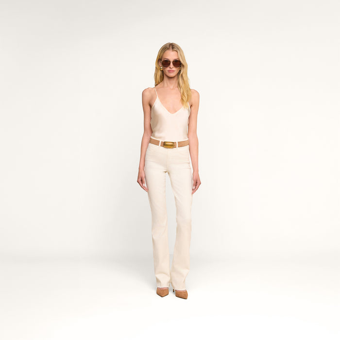 A woman wearing sunglasses, the Lexi Silk Camisole in pearl white, matching pants, a wide belt, and heels stands against a plain white background.