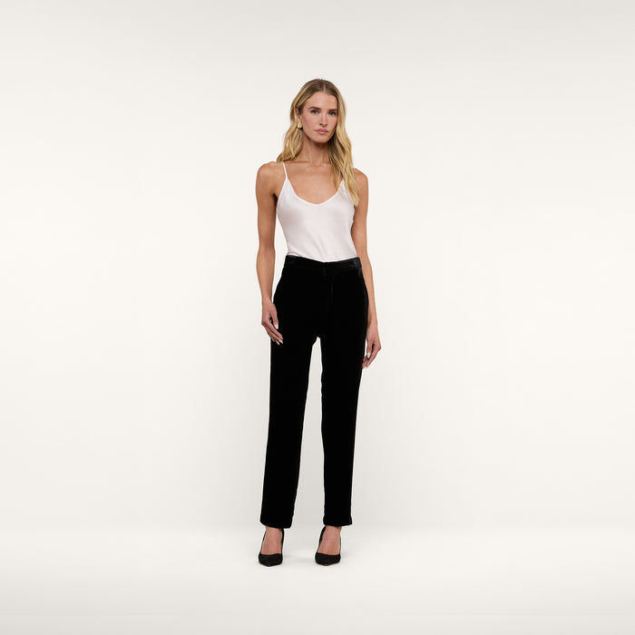 A woman stands facing forward against a plain white background, wearing the Lexi Silk Camisole—a white silk charmeuse top with adjustable straps—paired with black pants and black heels.