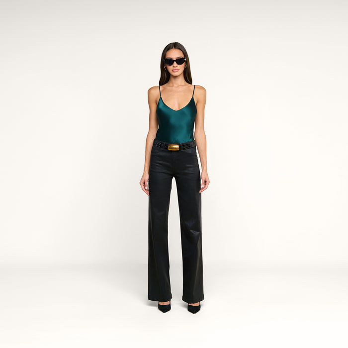 A woman wearing sunglasses, the Lexi Silk Camisole in teal with adjustable straps, black leather pants with a belt, and black heels stands against a plain white background.