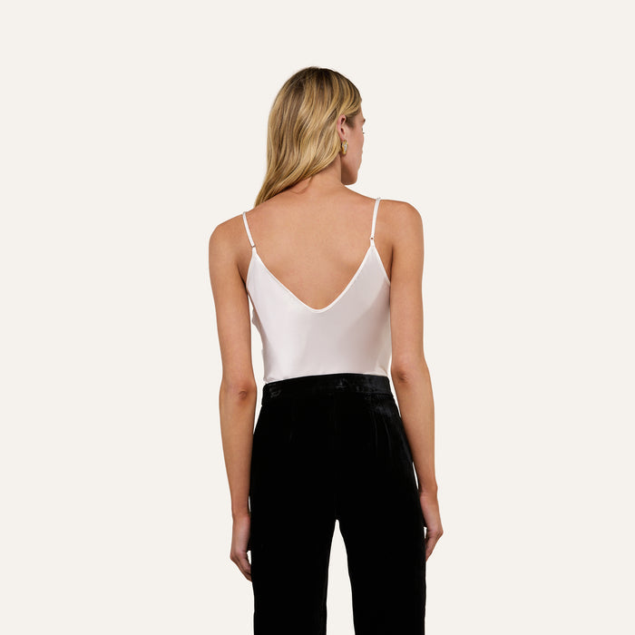A person with long blonde hair, dressed in the Lexi Silk Camisole with adjustable straps and black pants, is standing and facing away from the camera against a plain light background.