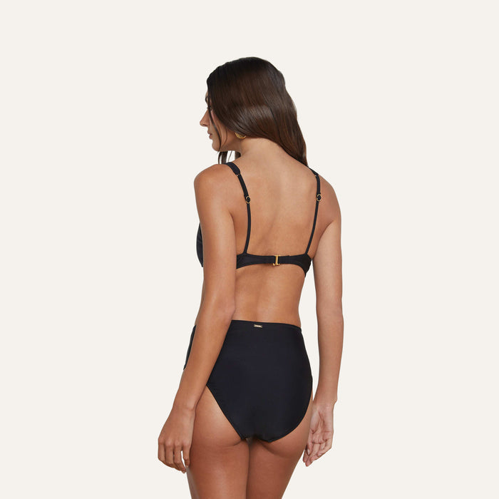A woman with long brown hair is shown from the back wearing the Lexie Bikini Top—a black bikini featuring a secure-fit top with adjustable straps, high-waisted bottoms, and gold coin hardware—standing against a plain light background.