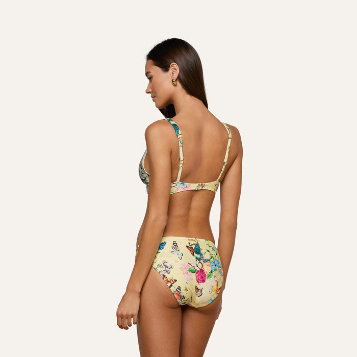 A woman with long brown hair wears the Lexie Bikini Top, which features a butterfly print and adjustable straps, standing with her back to the camera against a plain light background.