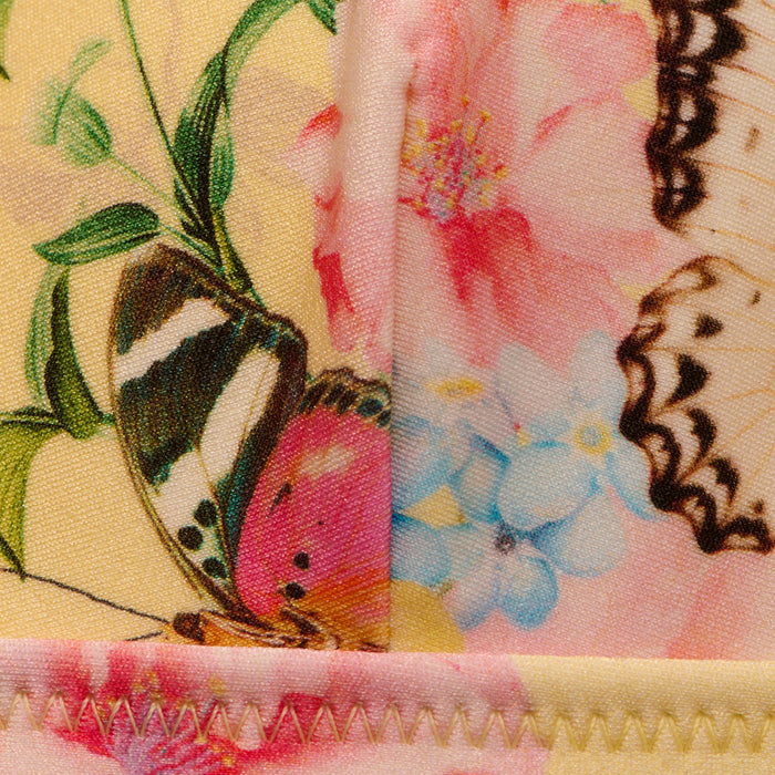 Close-up of the Lexie Bikini Top showcasing vibrant butterfly print and bright floral pattern, featuring pink, blue, and yellow flowers. The top displays visible stitching along the edge.