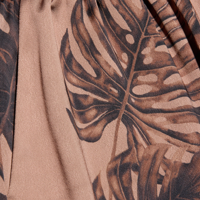 A close-up of the Lillian Satin Pant fabric, featuring a brown palm leaf print on a light pink background, highlighting the texture and detailed design.