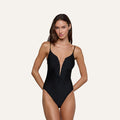 A woman wearing the Lilou One-Piece Swimsuit, featuring a black v-wire plunge and brass-chain straps, stands against a plain light background.