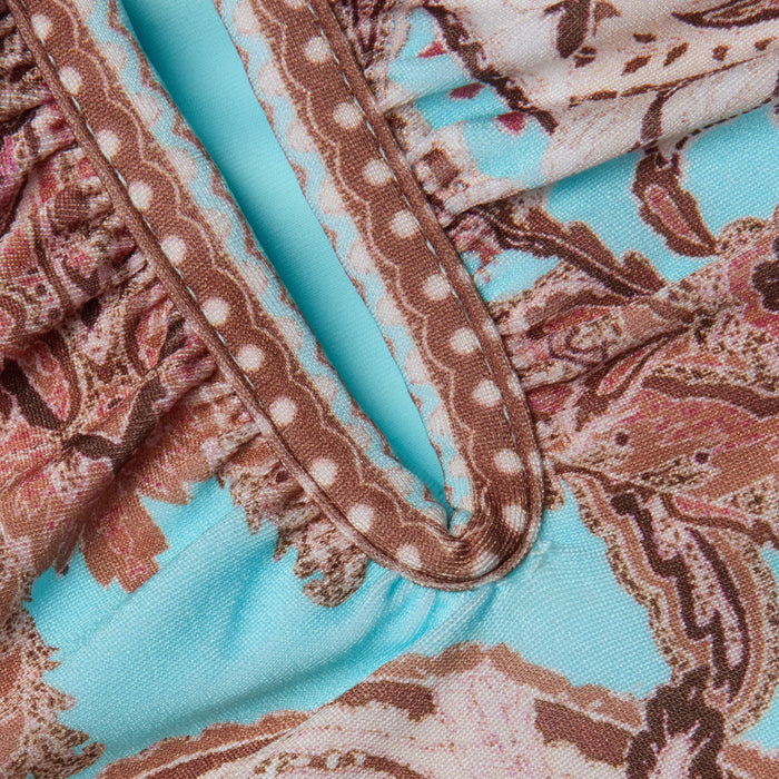 Close-up of the fabric from the Lilou One-Piece Swimsuit, showcasing a brown, pink, and cream floral and polka dot pattern on a light blue background, with gathered seams and decorative stitching.
