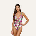 A woman wearing the Lisa Plunge One-Piece Swimsuit with a floral print and a deep V-neckline stands against a plain light background, one hand on her hip, looking at the camera.