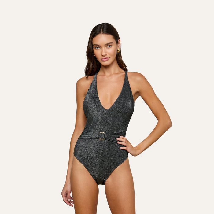 A woman wearing the Lisa Plunge One-Piece Swimsuit, a sparkly dark gray design featuring a plunging neckline and belted waist, stands against a plain light background.