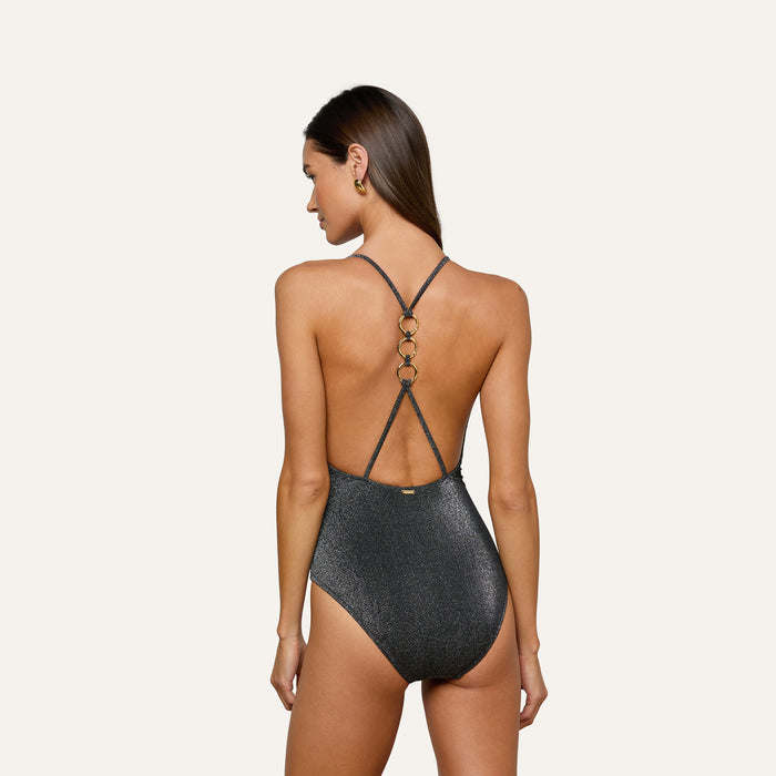 A woman is shown from behind, standing against a plain light background, wearing the Lisa Plunge One-Piece Swimsuit—an elegant, sparkly dark swimsuit with thin straps, gold ring accents on the back, and a subtle plunge neckline.
