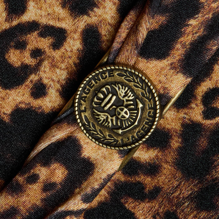 Close-up of a brass button engraved with “LAGENCE” alongside a laurel and peace sign design, sewn onto the leopard print fabric of the Lisa Plunge One-Piece Swimsuit.