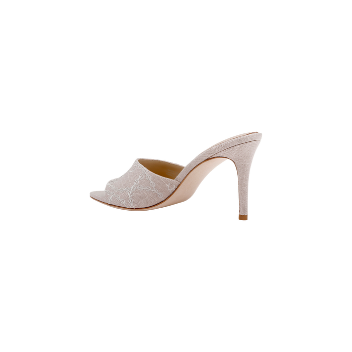 The Lolita Linen Open-Toe Mule in light beige features delicate white embroidery on embroidered linen, an open toe, and a slender stiletto heel, shown against a plain white background.
