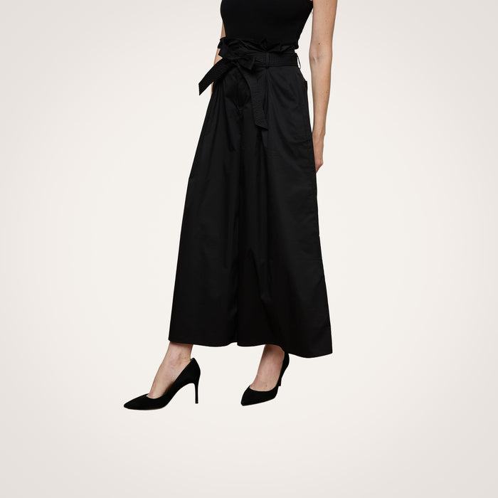 A person wears the Lowen Pant in black, styled with a sleeveless top and black high-heeled shoes. The lower half of the body is visible against a plain light background.