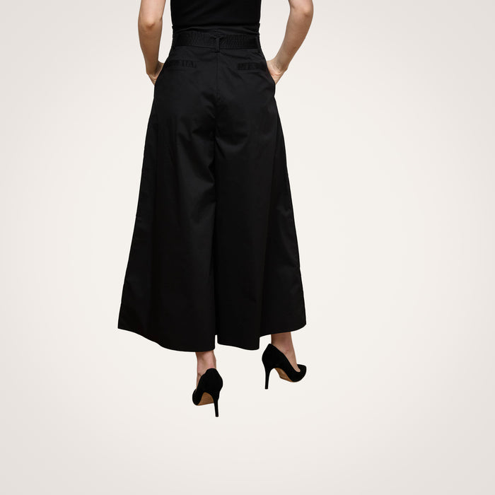 Wearing the Lowen Pant—high rise, wide-leg black poplin pants—with black high heels, the person is shown from the back against a plain light background. Their upper body is partially visible and their arms rest relaxed at their sides.