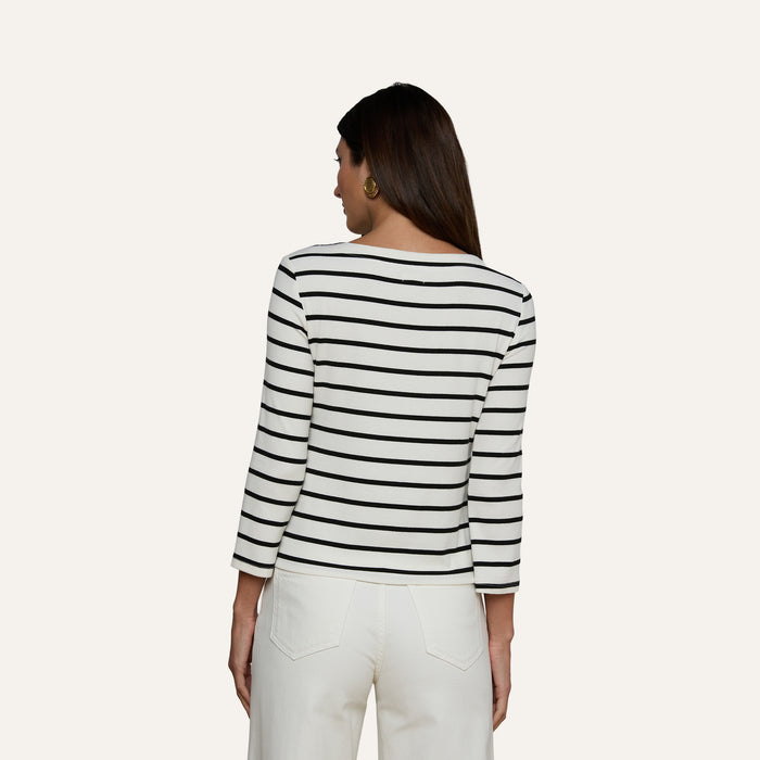A woman faces away, wearing the Lucille Striped Boatneck Top—its stretch modal fabric features classic black and white stripes and a flattering boat neckline—paired with white pants. Her dark hair is down against a light background, with the timeless stripes completing her look.