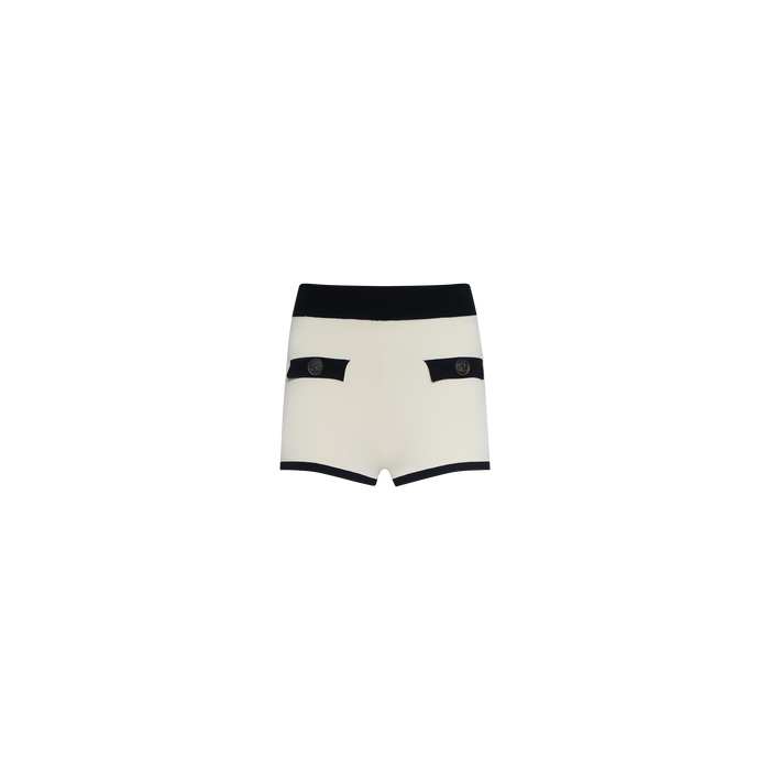 Lumi Knit Micro Short in white, designed with a black waistband and trim, crafted from power knit fabric. Features two front pockets accented with black flaps and decorative buttons, shown against a plain white background.