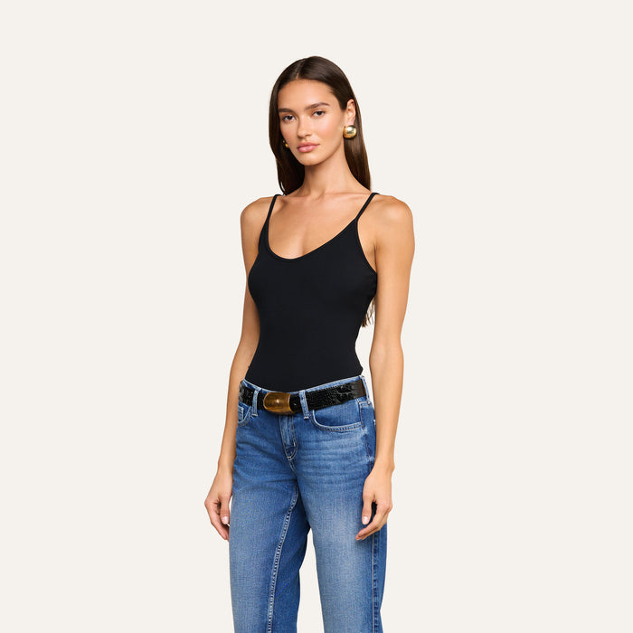 Woman wearing a black Lunara Camisole made from ribbed fabric, blue jeans with a black belt, and gold earrings, standing against a plain light background.