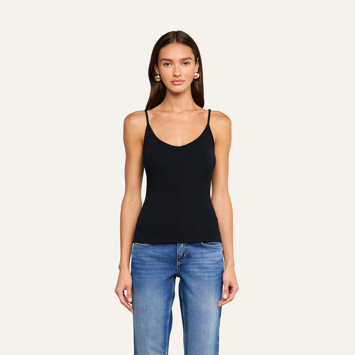 A woman with long brown hair, wearing a black ribbed Lunara Camisole and blue jeans, stands facing forward against a plain light background.