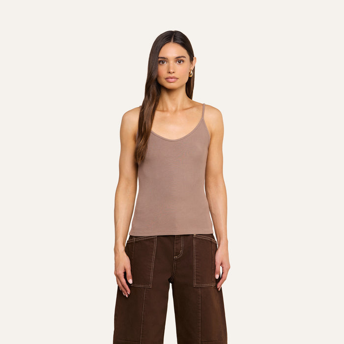 A woman with long brown hair stands facing forward against a plain light background, wearing a beige Lunara Camisole crafted from ribbed fabric and brown wide-leg pants.