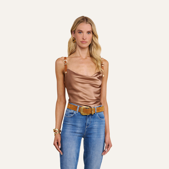 A woman wearing the Lux Silk Buckle-Strap Camisole in bronze, styled with blue jeans, a tan belt, and gold jewelry stands against a plain light background.