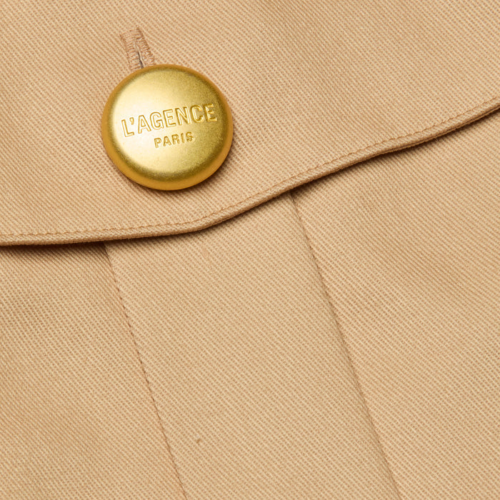 Close-up of the Maelis Mini Skirt in beige, featuring a gold button engraved with LAGENCE PARIS near the seam and flap, highlighting the tailored detail of this high-rise waist design.