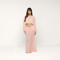 A woman stands in a light pink, long-sleeve crop top and the Mahe Mesh Cover-Up Skirt, styled as a matching set that channels poolside elegance. She faces forward with a neutral expression against a plain white background.