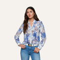 A woman wears the Maia Lace Blouse in navy floral, paired with blue jeans and a white belt, standing with her hands in her pockets against a plain light background.