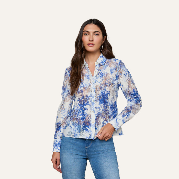 Woman wearing the Maia Lace Blouse— a navy floral long-sleeve top featuring chevron lace details—paired with light blue jeans, standing against a plain light background.