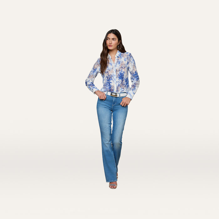 A woman stands facing forward against a plain white background, wearing the Maia Lace Blouse in navy floral, paired with light blue jeans, a black belt, and sandals.