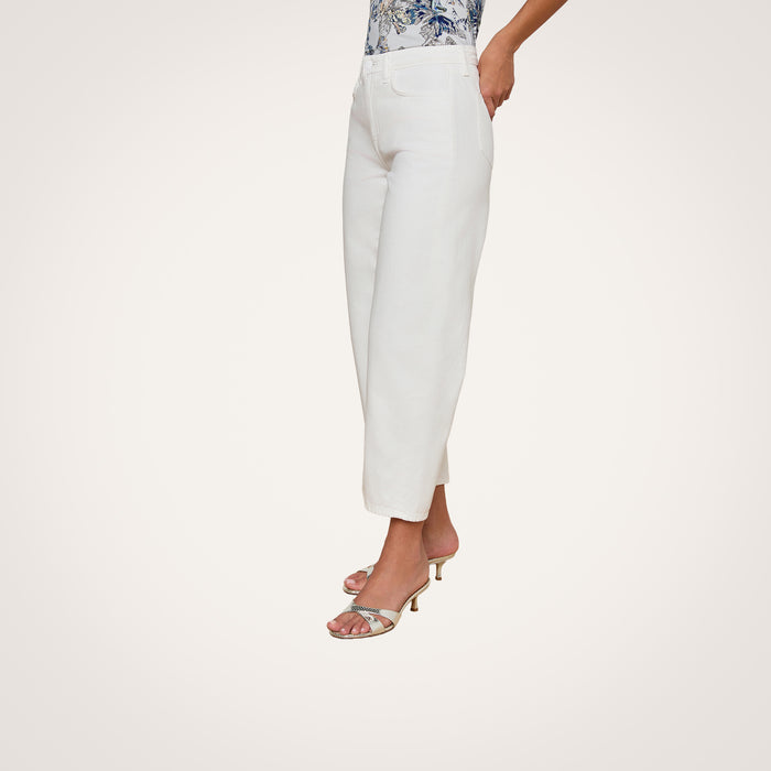 Wearing the Mallis Bow-Leg Jean in white—styled with a floral top and open-toe heeled sandals—a person stands against a plain background.