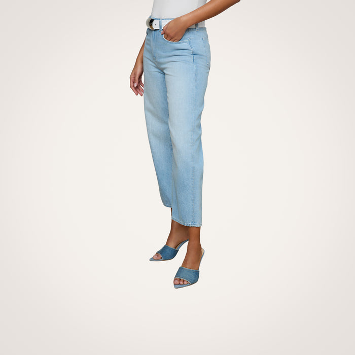 Woman wearing the Mallis Bow-Leg Jean in a light wash with a high rise and straight-leg fit, paired with a white top and blue open-toe heeled sandals, standing against a plain white background. Only the lower half of her body is visible.