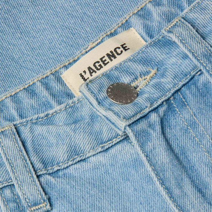 Close-up of the Mallis Bow-Leg Jean in light wash denim, showcasing a silver button and a visible white LAGENCE label with black text inside the waistband.