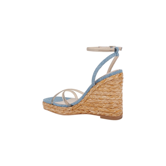 The Malone Wedge Espadrille is a bohemian espadrille wedge sandal featuring a braided straw sole, light blue fabric upper, thin white straps, and an ankle strap with a silver buckle. It includes a comfortable memory foam insole and is shown in profile against a white background.
