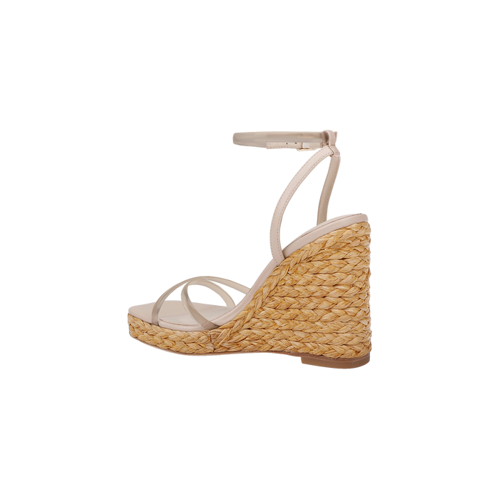 The Malone Wedge Espadrille is a beige strappy sandal with a high raffia wedge heel crafted from woven straw, featuring an ankle strap and a slightly open toe, shown against a white background for an effortless bohemian style look.