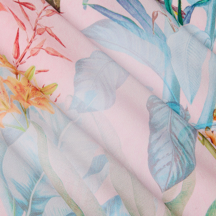 A close-up of the Marena Sarong reveals its pastel floral pattern with blue, orange, and green leaves and flowers on a soft pink background. The material features gentle folds, a smooth texture, and is perfect for creating a stylish beach cover-up or sarong.