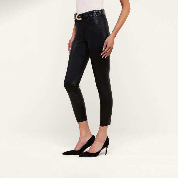 A person wearing the Margot Coated Cropped Skinny Jean, a light top, a black belt with a gold buckle, and black high-heeled shoes poses against a plain white background.