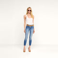 A woman wearing sunglasses, a white tank top, the Margot Cropped Skinny Jean crafted from premium stretch denim, and brown high heels stands against a plain white background.