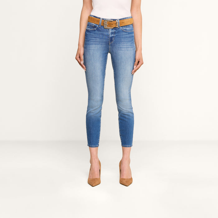 A person wearing a white top, the Margot Cropped Skinny Jean—high-rise skinny jeans crafted from premium stretch denim with sustainable recycled fiber—a brown belt, and brown pointed high heels stands against a plain white background.