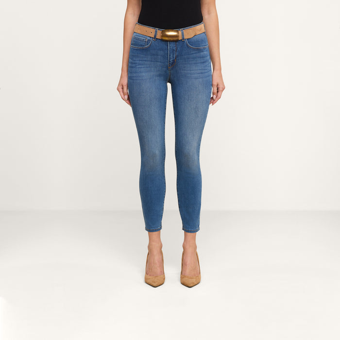 Wearing the Margot Cropped Skinny Jean in stretch denim with a vintage blue wash, styled with a brown belt, black top, and tan high heels, standing against a plain white background.