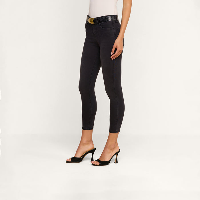Wearing the Margot Cropped Skinny Jean in black, a person with a white top, black belt, and black high-heeled sandals stands against a plain white background.