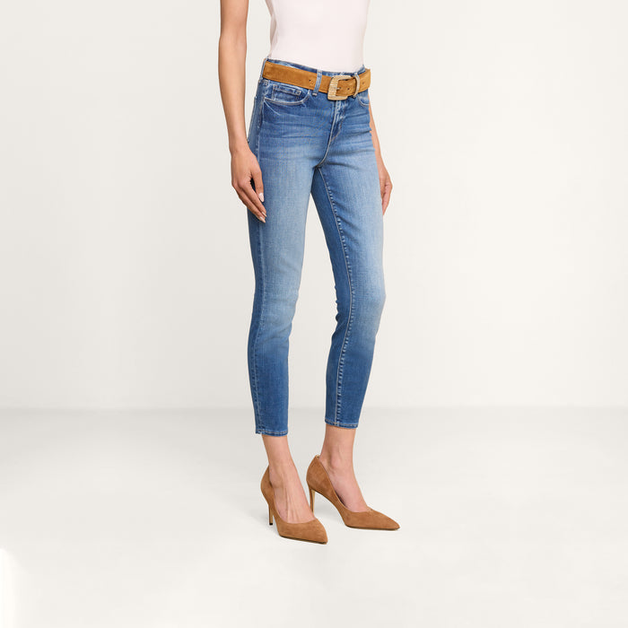 A person wearing the Margot Cropped Skinny Jean, crafted from premium stretch denim, paired with a tan belt, a sleeveless white top, and tan high heels, stands against a plain light background. Only the lower body is visible.