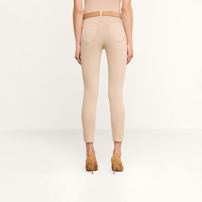 A person stands facing away against a plain white background, wearing Margot Cropped Skinny Jeans in beige stretch denim, styled with a matching belt and tan high-heeled shoes.