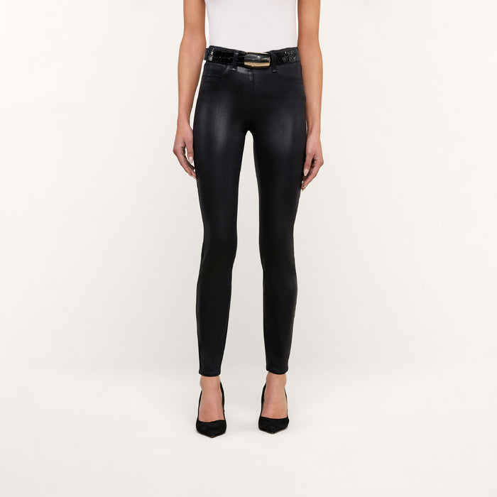 Wearing the Marguerite Coated Skinny Jean, a black belt, a white sleeveless top, and black heels, the person stands against a plain white background.