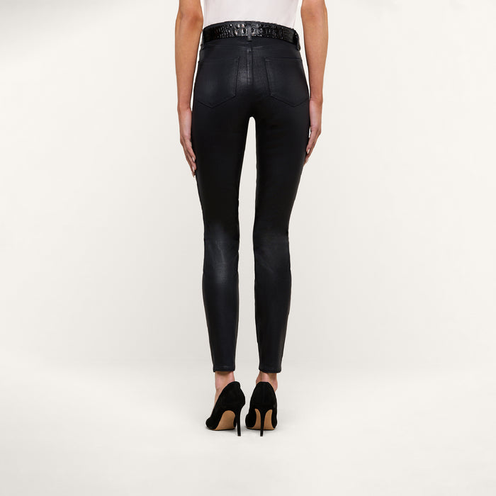 A person stands facing away from the camera, wearing the Marguerite Coated Skinny Jean in black, paired with black high-heeled shoes and a white top against a plain white background.